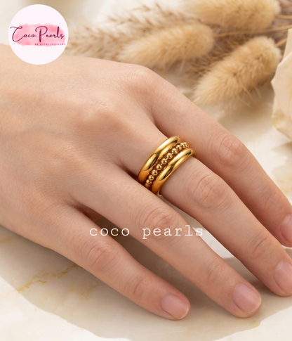 Coco pearls stainless Steel anti tarnish close-up of a hand wearing three stacked gold ring, with two plain sides and beaded chain in center 