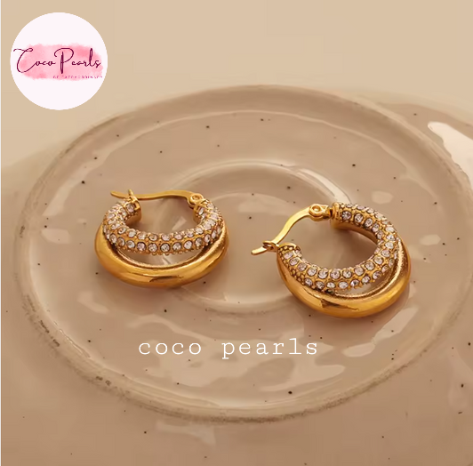 Coco pearls stainless Steel anti tarnish pair of gold crescent hoop earrings with rows of clear pavé stones, displayed on a speckled beige ceramic dish.