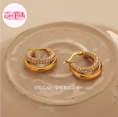Coco pearls stainless Steel anti tarnish pair of gold crescent hoop earrings with rows of clear pavé stones, displayed on a speckled beige ceramic dish.