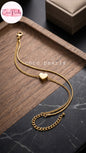 Coco pearls stainless Steel anti tarnish gold chain bracelet with a small heart charm, displayed on a wooden tray over a dark marble surface.