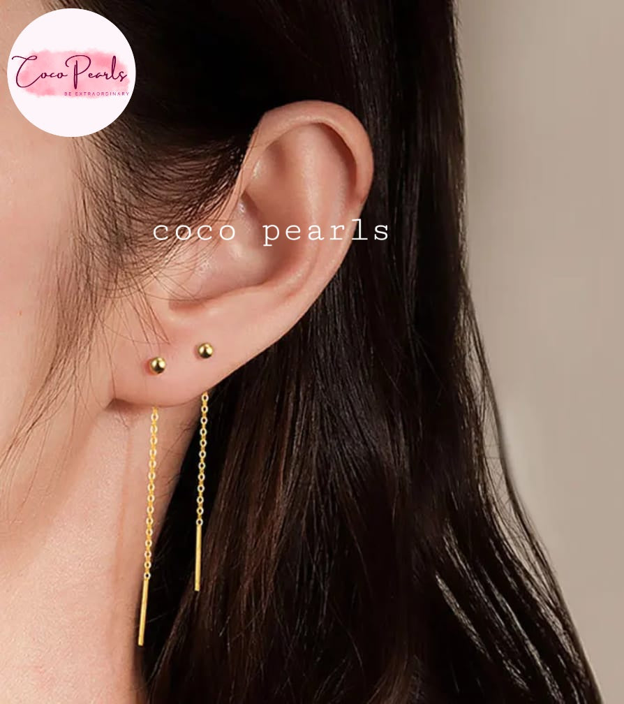 Coco pearls stainless Steel anti tarnish close-up of a person's ear wearing two gold stud earrings, one of which has a long dangling chain with a thin vertical bar. 