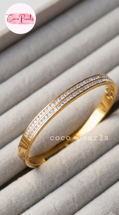 Coco pearls stainless Steel gold bangle bracelet with two rows of clear pavé stones, displayed on a light gray velvet jewelry organizer.
