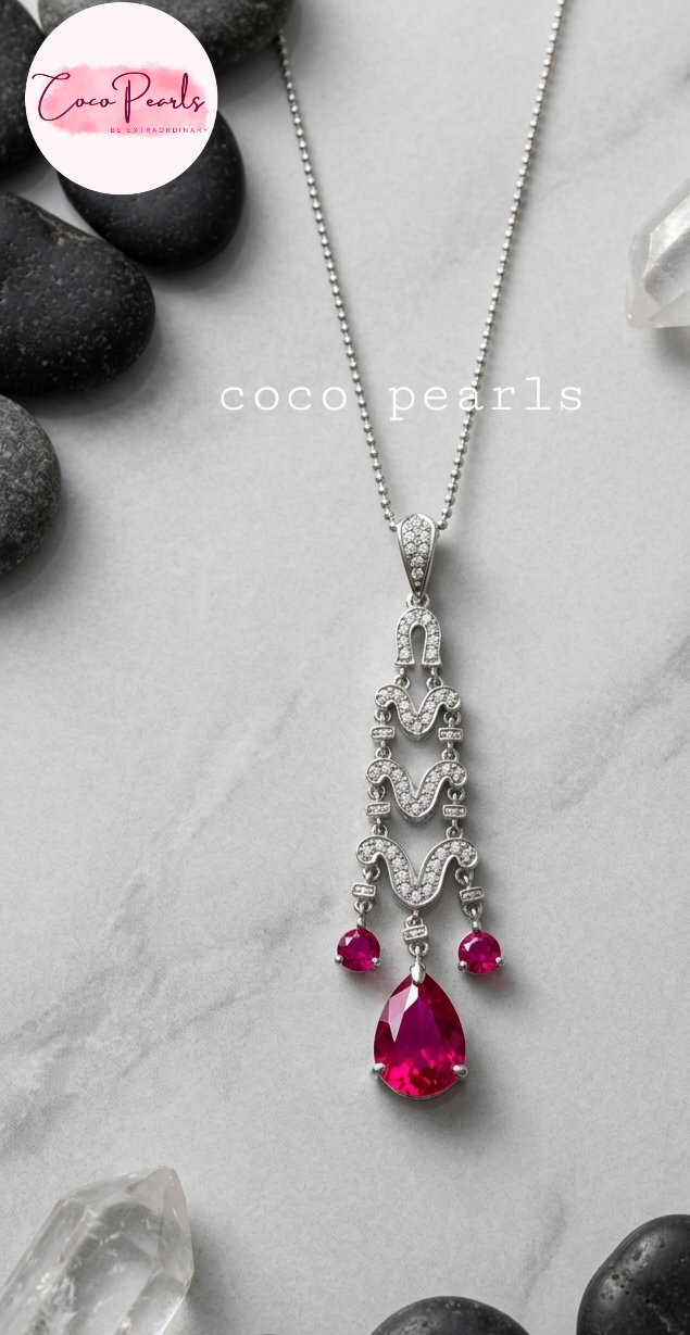 Elegant necklace with red gemstones on a gray surface with 'Coco Pearls' branding.