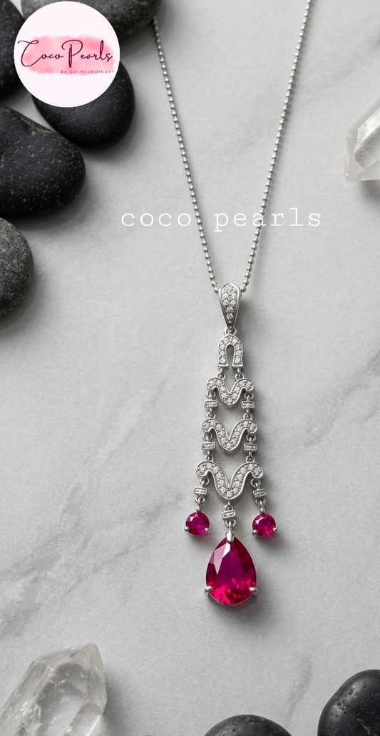 Elegant necklace with red gemstones on a gray surface with 'Coco Pearls' branding.