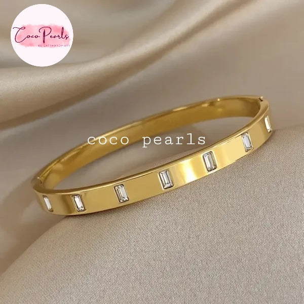 Coco pearls stainless Steel anti tarnish Gold eternity line handcuff bracelet with embedded stones on a beige fabric 