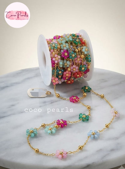 Coco pearls stainless Steel anti tarnish spool of colorful beaded flower garland with a matching draped chain necklace displayed on a white marble surface. The beads are in pink, green, teal, and light blue with gold-toned chain links.