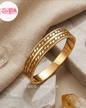 Coco pearls stainless Steel anti tarnish gold bangle bracelet with a raised chain-link pattern, displayed on a textured beige fabric and stone surface.