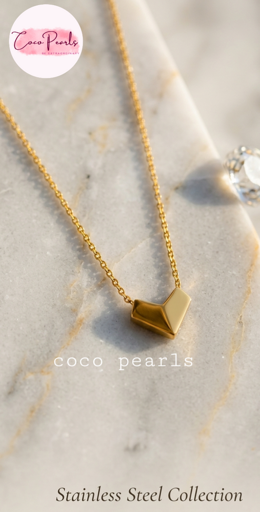Gold necklace with a geometric pendant on a marble surface, branded 'Coco Pearls'.