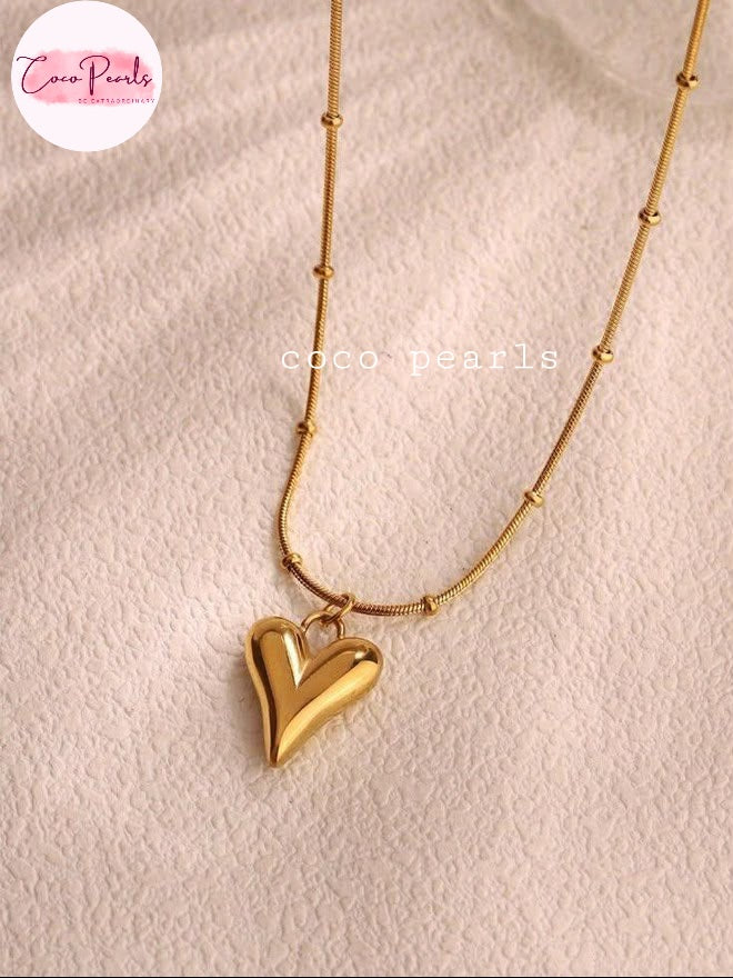 Coco pearls stainless Steel anti tarnish gold beaded chain necklace with a polished gold heart pendant, displayed on a textured light pink fabric background.
