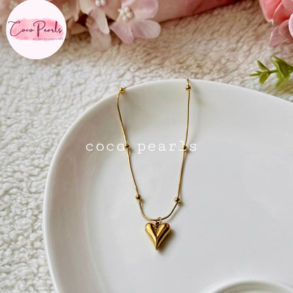 Coco pearls stainless Steel anti tarnish delicate gold chain necklace with a small heart-shaped pendant, displayed on a white plate. The necklace features small gold beads along the chain.