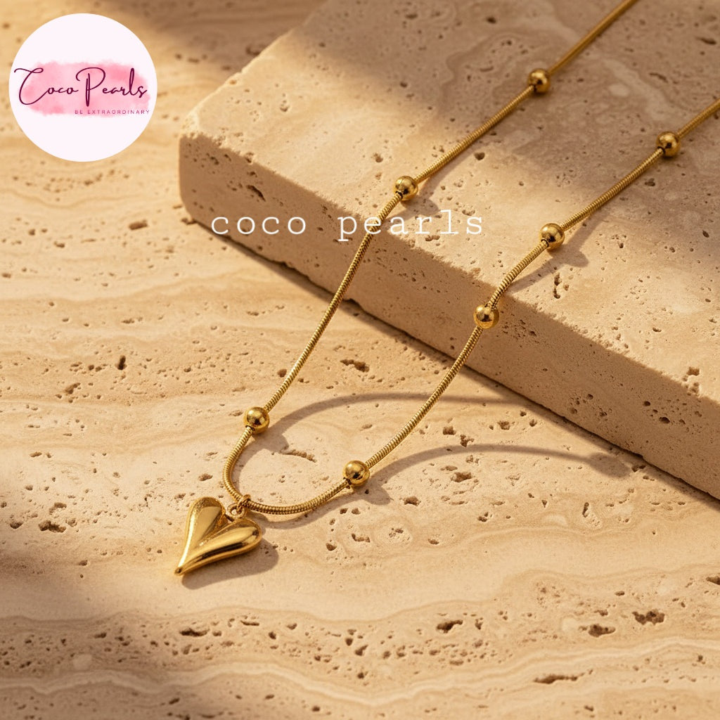 Coco pearls stainless Steel anti tarnish gold chain necklace with small bead accents and a polished heart pendant, styled on a beige stone surface with a matching stone block. 