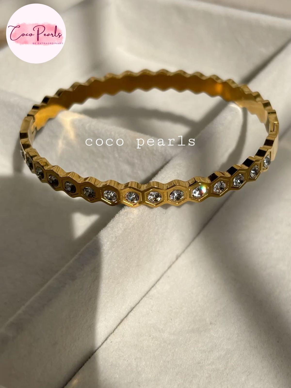 Coco pearls stainless Steel anti tarnish gold bangle bracelet with a scalloped edge and small clear rhinestones set along the front, displayed on a white fabric.