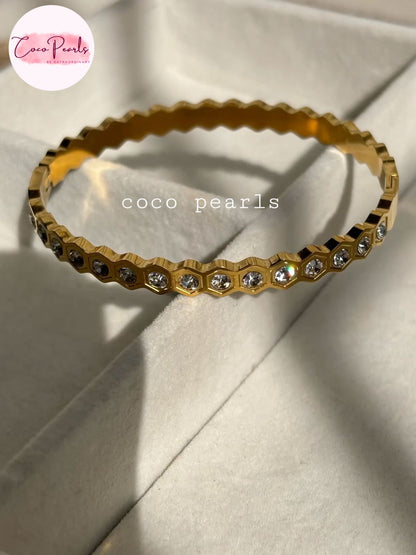 Coco pearls stainless Steel anti tarnish gold bangle bracelet with a scalloped edge and small clear rhinestones set along the front, displayed on a white fabric.