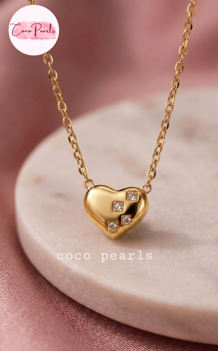 Coco pearls stainless Steel anti tarnish gold heart-shaped pendant necklace with three small clear gemstones, displayed on a light pink marble