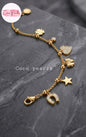 Coco pearls stainless Steel anti tarnish bracelet with various charms including a horseshoe, star, clover, heart, and flower, displayed on a dark gray marble surface.