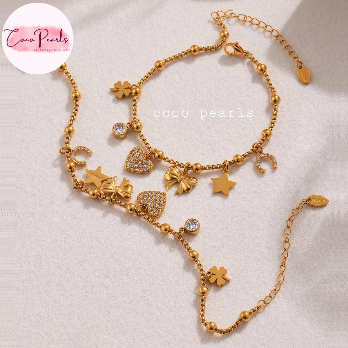 Coco pearls stainless Steel anti tarnish gold-toned beaded anklet with multiple charms including stars, hearts, flowers, and crescent moons, displayed on a textured white fabric background.
