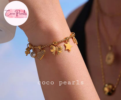 Coco pearls stainless Steel anti tarnish gold charm bracelet with a clover, heart, bow, and star design, shown on a person's wrist against a blue sky background. 