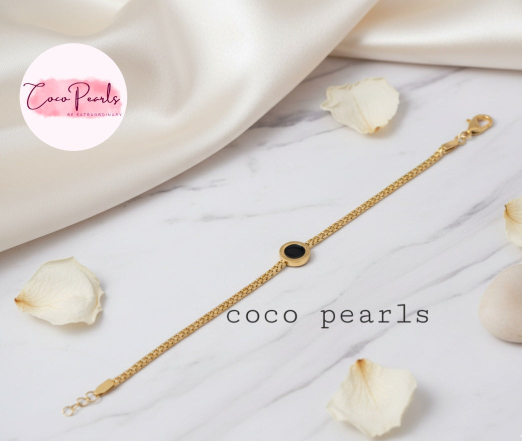 Coco Pearls Stainless Steel Anti tarnish Gold midnight aura bracelet with a black circle charm on mesh chain on a white fabric background