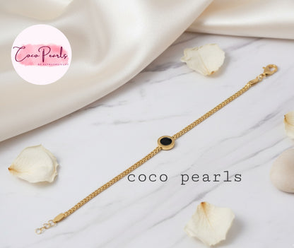 Coco Pearls Stainless Steel Anti tarnish Gold midnight aura bracelet with a black circle charm on mesh chain on a white fabric background