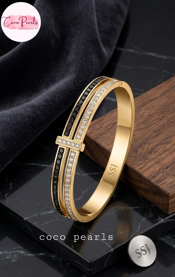 Coco pearls stainless Steel anti tarnish Gold bangle bracelet with black and crystal accents, displayed on a dark marble surface with a wooden block