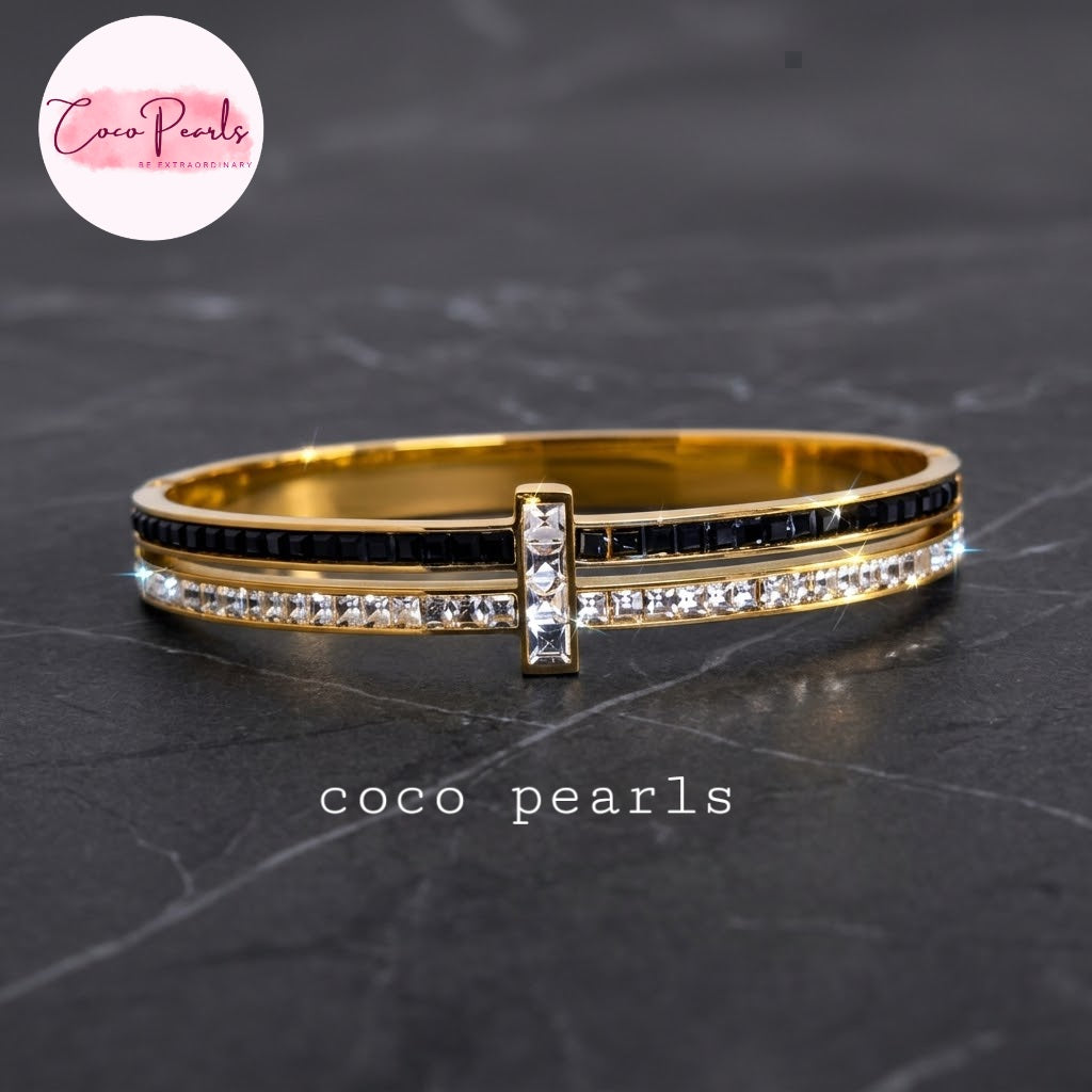 Coco pearls stainless Steel anti tarnish gold-plated hinged bangle bracelet with a central cross-shaped charm, featuring one row of black stones and another row of clear rhinestones.