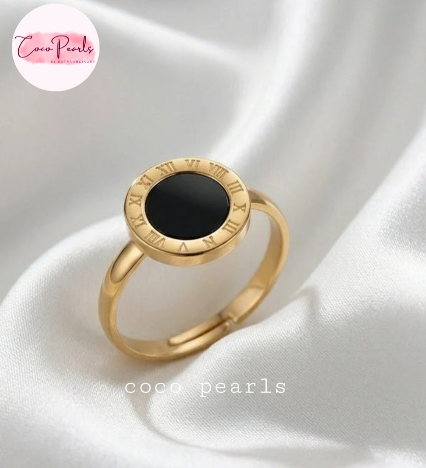 Coco pearls stainless Steel anti tarnish gold signet-style ring with a round black inlay and Roman numeral detailing around the bezel, displayed on white satin fabric.