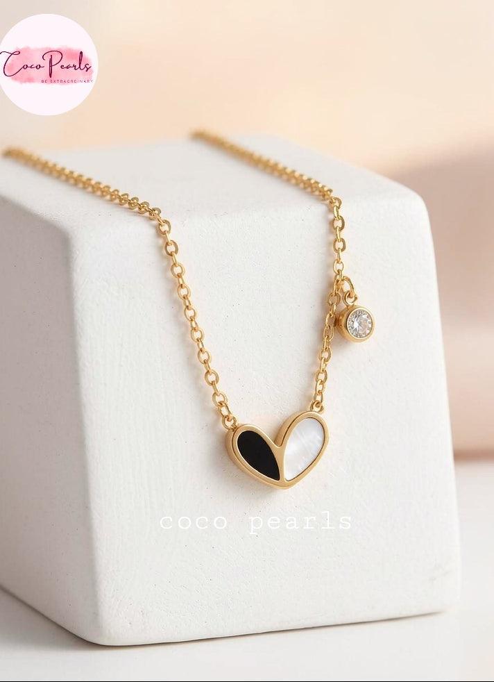 Coco pearls stainless Steel anti tarnish gold chain necklace with a heart-shaped pendant split into black and white halves, displayed on a white jewelry block.