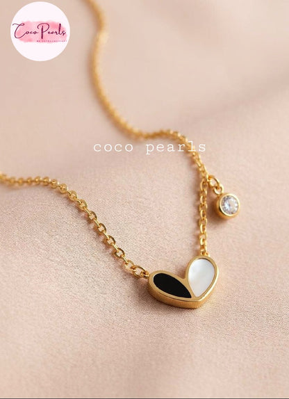Coco pearls stainless Steel anti tarnish gold chain necklace with a heart-shaped pendant featuring black and white enamel inlay, plus a small round clear stone charm, displayed on a soft beige background.