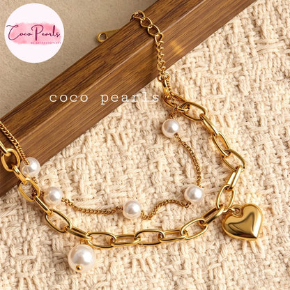 Coco pearls stainless Steel anti tarnish gold-tone layered chain bracelet with white faux pearls and a polished heart charm, displayed on a textured cream fabric