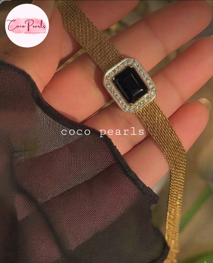 Coco pearls stainless Steel anti tarnish gold mesh bracelet with a rectangular black gemstone and a diamond-encrusted border, held in a hand. 