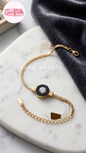 Coco pearls stainless Steel anti tarnish gold chain bracelet with a central octagonal black and gold charm featuring a clear crystal, displayed on a white marble tray with a dark gray velvet cloth.