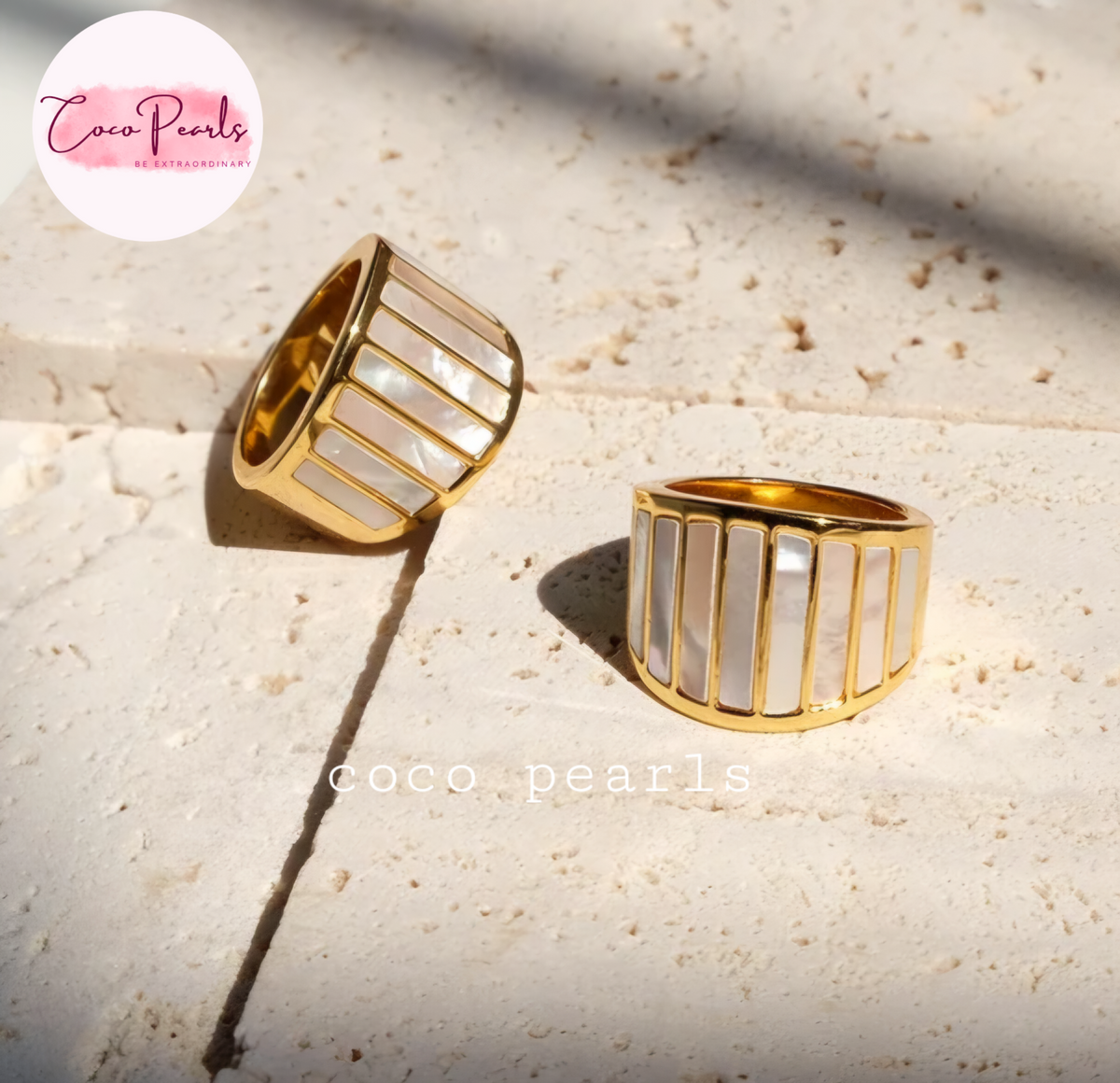 Coco pearls stainless Steel anti tarnish Two gold-plated rings with vertical white mother-of-pearl inlay panels, displayed on a textured beige stone surface