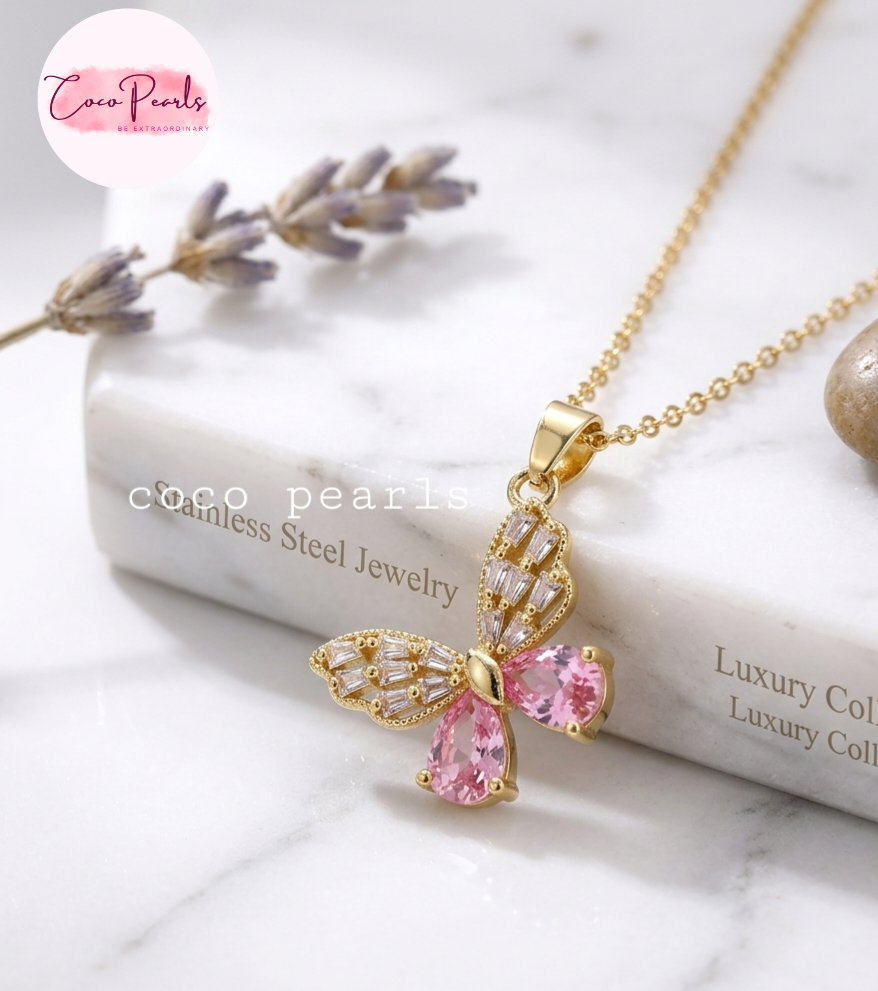 Coco pearls stainless Steel anti tarnish Gold butterfly pendant necklace with pink teardrop gemstones and clear crystal accents, displayed on a white marble surface with a book and lavender sprigs.