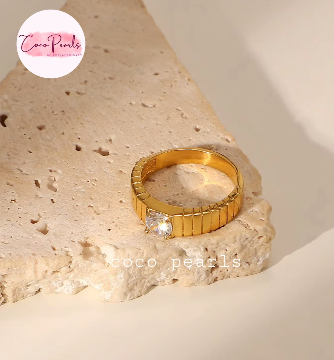 Coco pearls stainless Steel anti tarnish gold ring with a textured, ribbed band and a single clear round gemstone, displayed on a beige stone slab. 