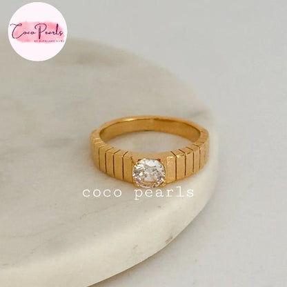 Coco pearls stainless Steel anti tarnish gold ring with a textured, ribbed band and a single round clear gemstone, displayed on a white marble slab.