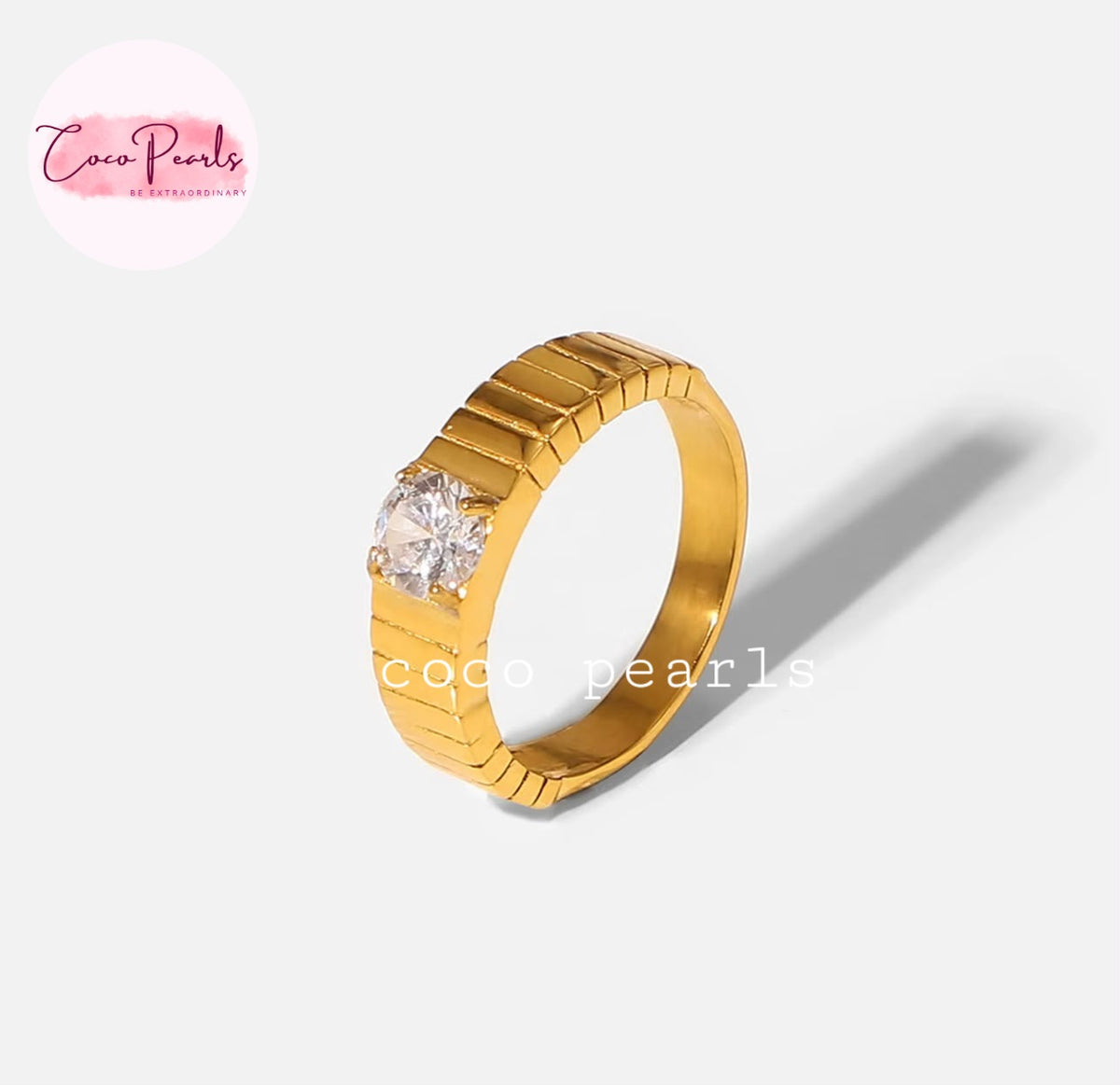 Coco pearls stainless Steel anti tarnish gold ring with a textured, ribbed band and a single round clear gemstone in a bezel setting, shown on a light gray background with a soft shadow. 