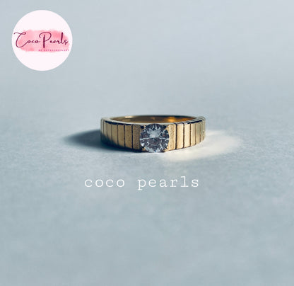 Coco pearls stainless Steel anti tarnish gold ring with a textured, ribbed band and a single round clear gemstone, displayed on a light gray surface.