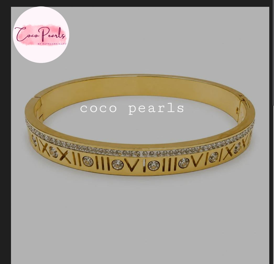 Coco pearls stainless Steel anti tarnish gold bangle bracelet with Roman numerals and clear rhinestones, shown on a gray background 