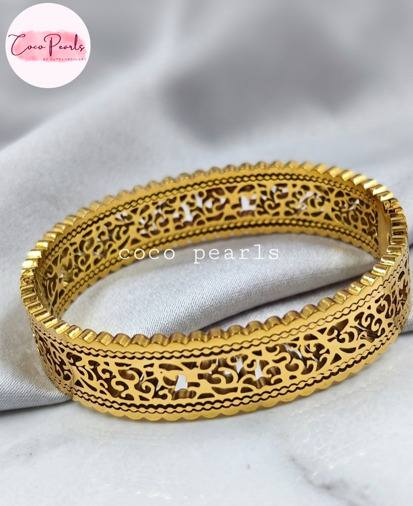 Coco pearls stainless Steel anti tarnish gold-plated filigree bangle bracelet with intricate cut-out patterns, displayed on a soft white fabric background.