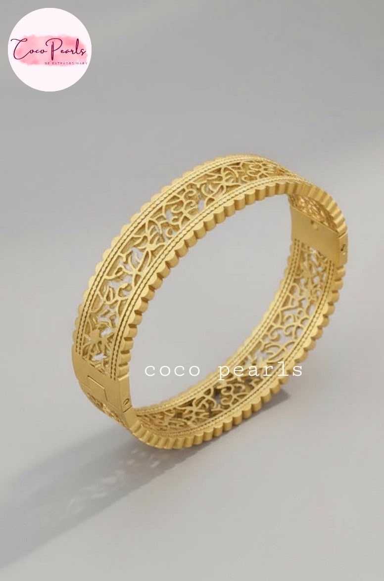 Coco pearls stainless Steel anti tarnish gold filigree bangle bracelet with intricate cut-out patterns and a textured beaded edge, displayed on a neutral gray background.