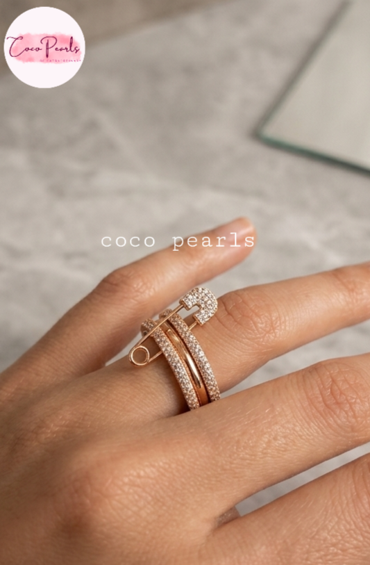 Coco pearls stainless Steel anti tarnish close-up of a hand wearing a rose gold ring with a pavé-set square bezel and a safety-pin style band, on a light gray marble surface.