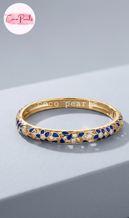 Coco pearls gold-plated bangle bracelet with blue enamel and small clear stones, displayed on a light gray surface.