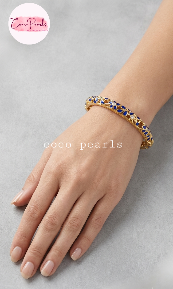 Coco pearls gold-plated bangle bracelet with blue and white enamel detailing, worn on a model's wrist against a neutral gray background.