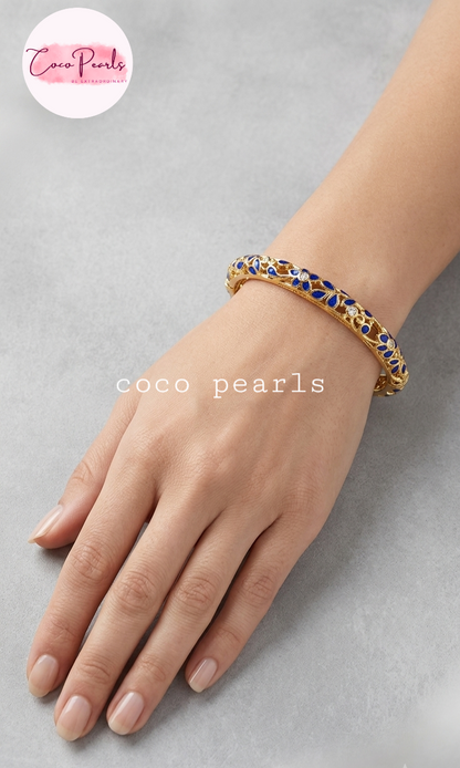 Coco pearls gold-plated bangle bracelet with blue and white enamel detailing, worn on a model's wrist against a neutral gray background.