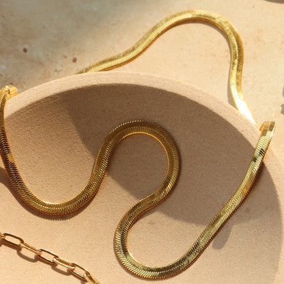 Coco pearls stainless Steel anti tarnish close-up of a gold snake chain draped over a beige textured surface, with a matching gold chain link visible in the lower left corner.