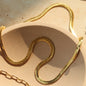 Coco pearls stainless Steel anti tarnish close-up of a gold snake chain draped over a beige textured surface, with a matching gold chain link visible in the lower left corner.