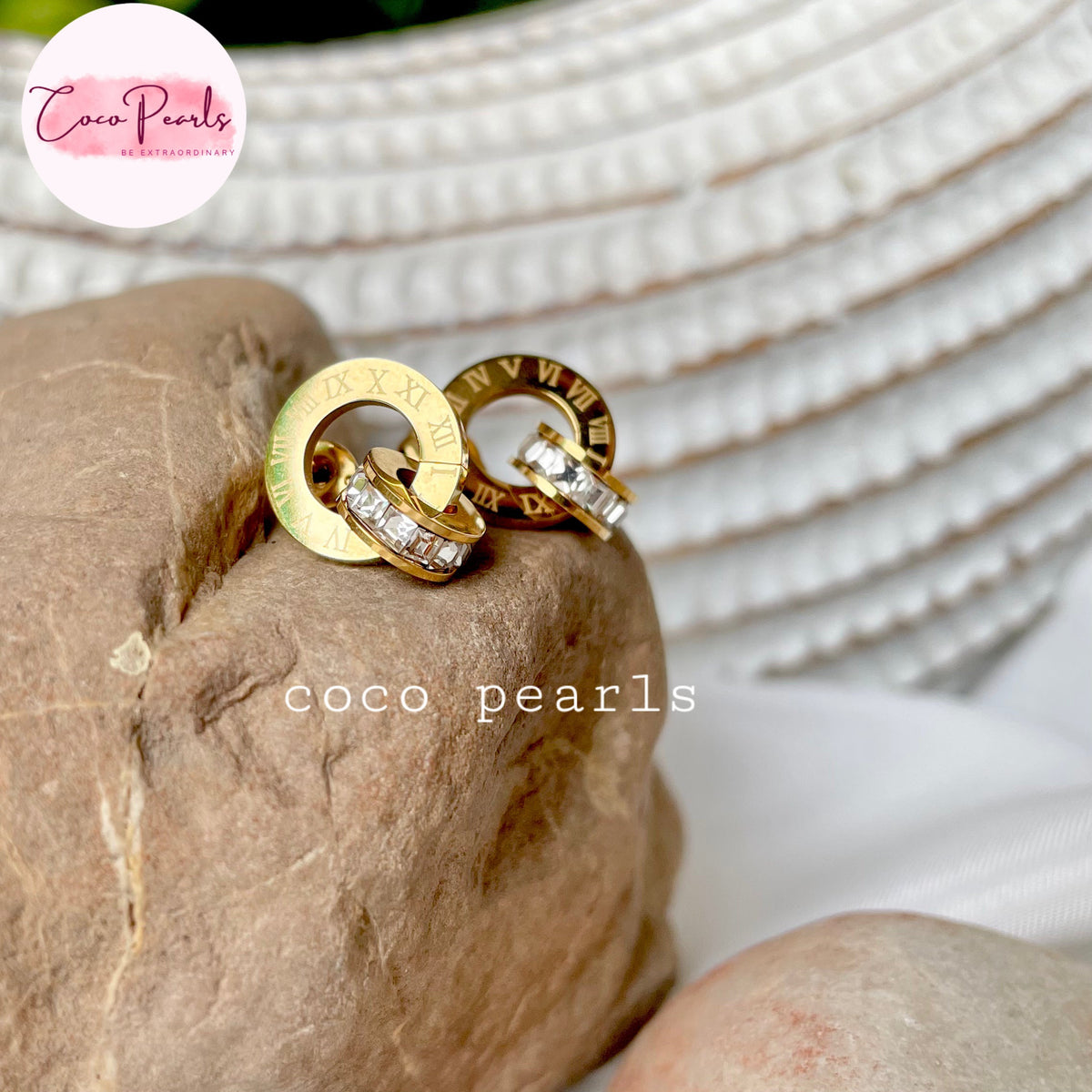 Coco pearls stainless Steel anti tarnish pair of gold-tone ring earrings with Roman numerals and clear stones, displayed on a textured brown stone