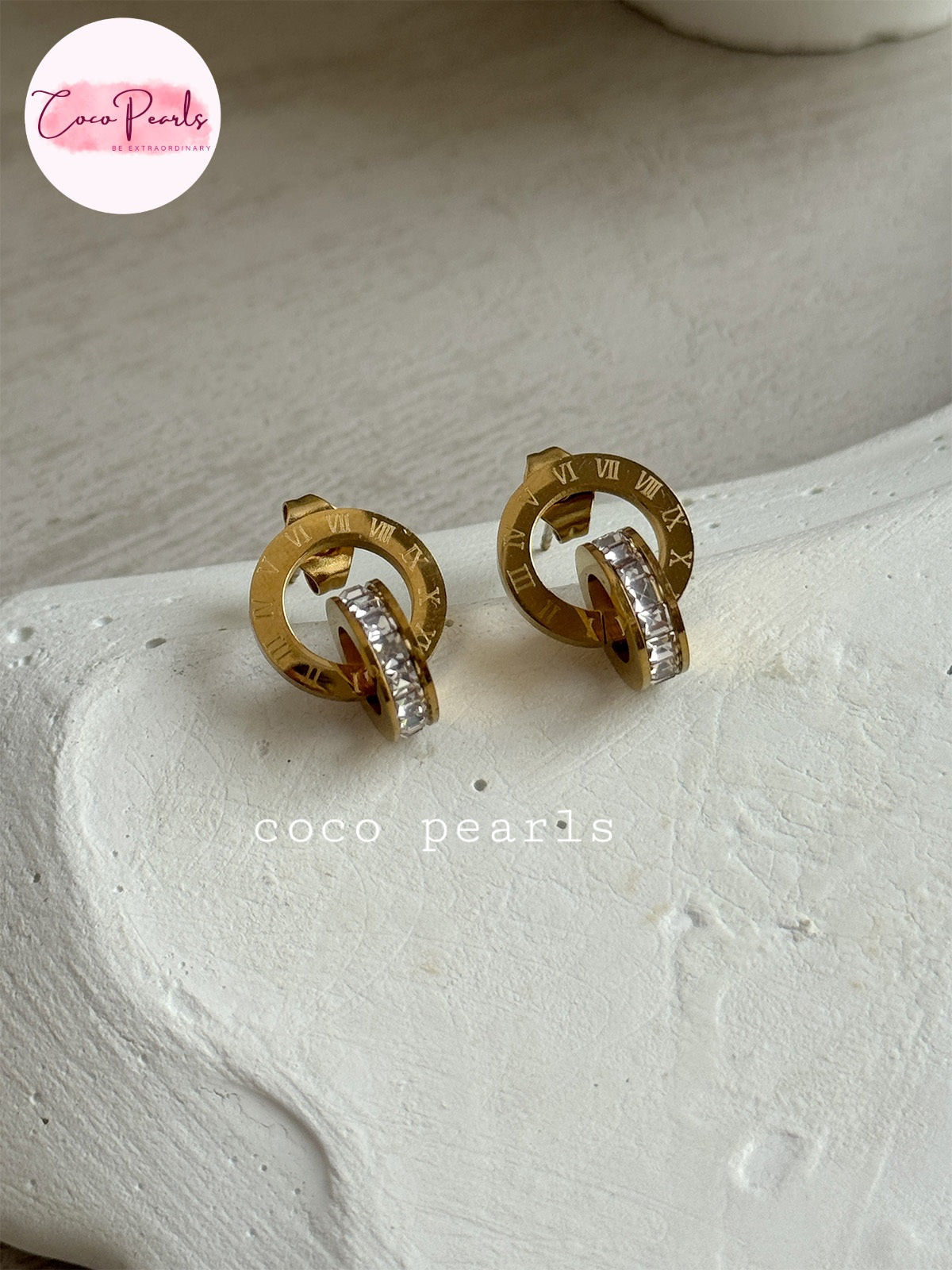 Coco pearls stainless Steel anti tarnish pair of gold-toned hoop earrings with clear rhinestone accents, displayed on a textured white surface. 