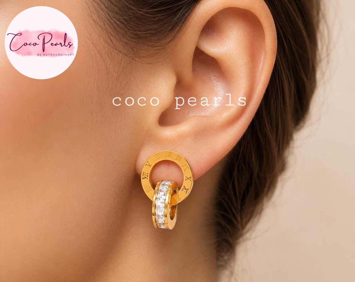 Coco pearls stainless Steel anti tarnish close-up of a model's ear wearing a gold double-hoop earring with Roman numerals and a row of clear pavé stones. 