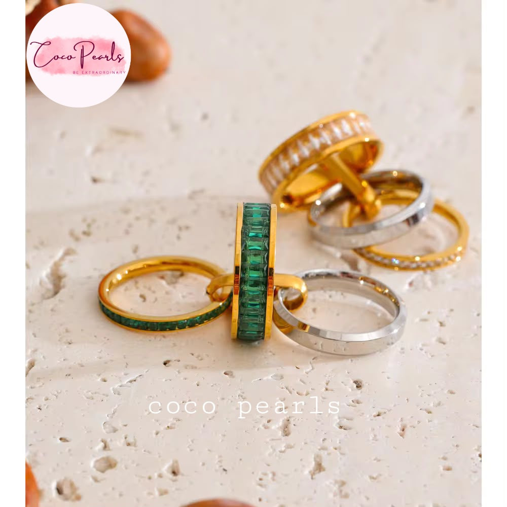 Coco pearls stainless Steel anti tarnish set of gold and silver rings with emerald-cut green stones, displayed on a textured beige stone surface.